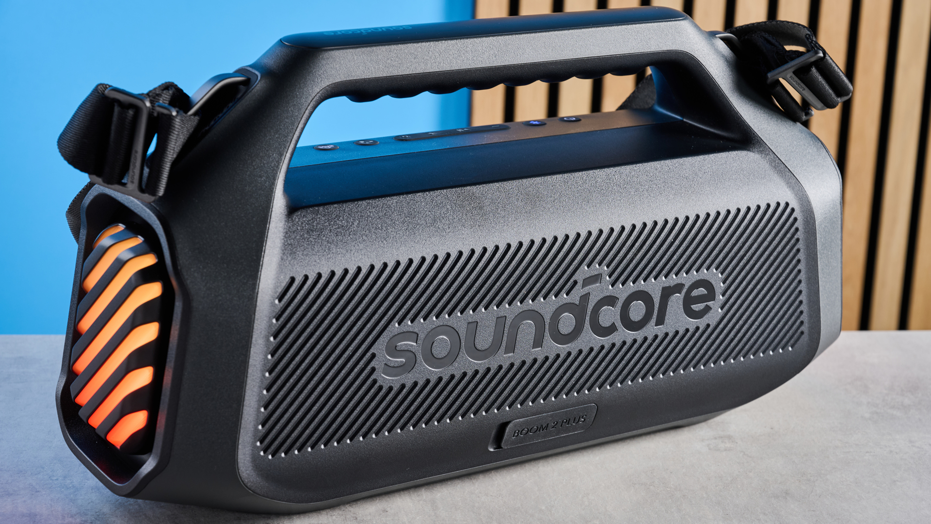 the soundcore boom 2 plus boombox speaker with LED lights and a black mesh casing with buttons for BassUp and light show and a carry handle and strap