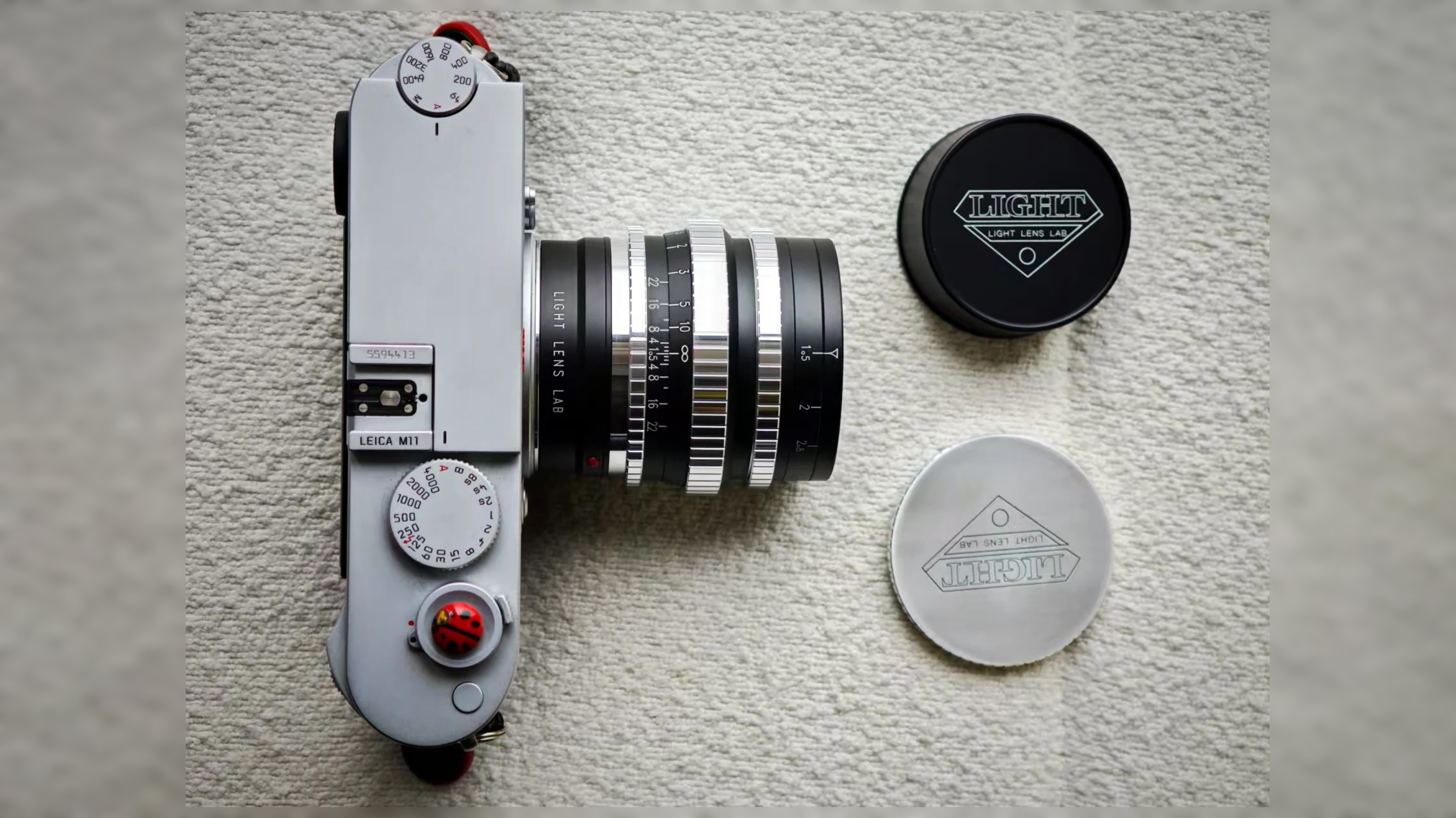A vintage Leica camera with a Light Lens Lab lens the 50mm f/1,5, accompanied by lens caps, laid on a textured surface