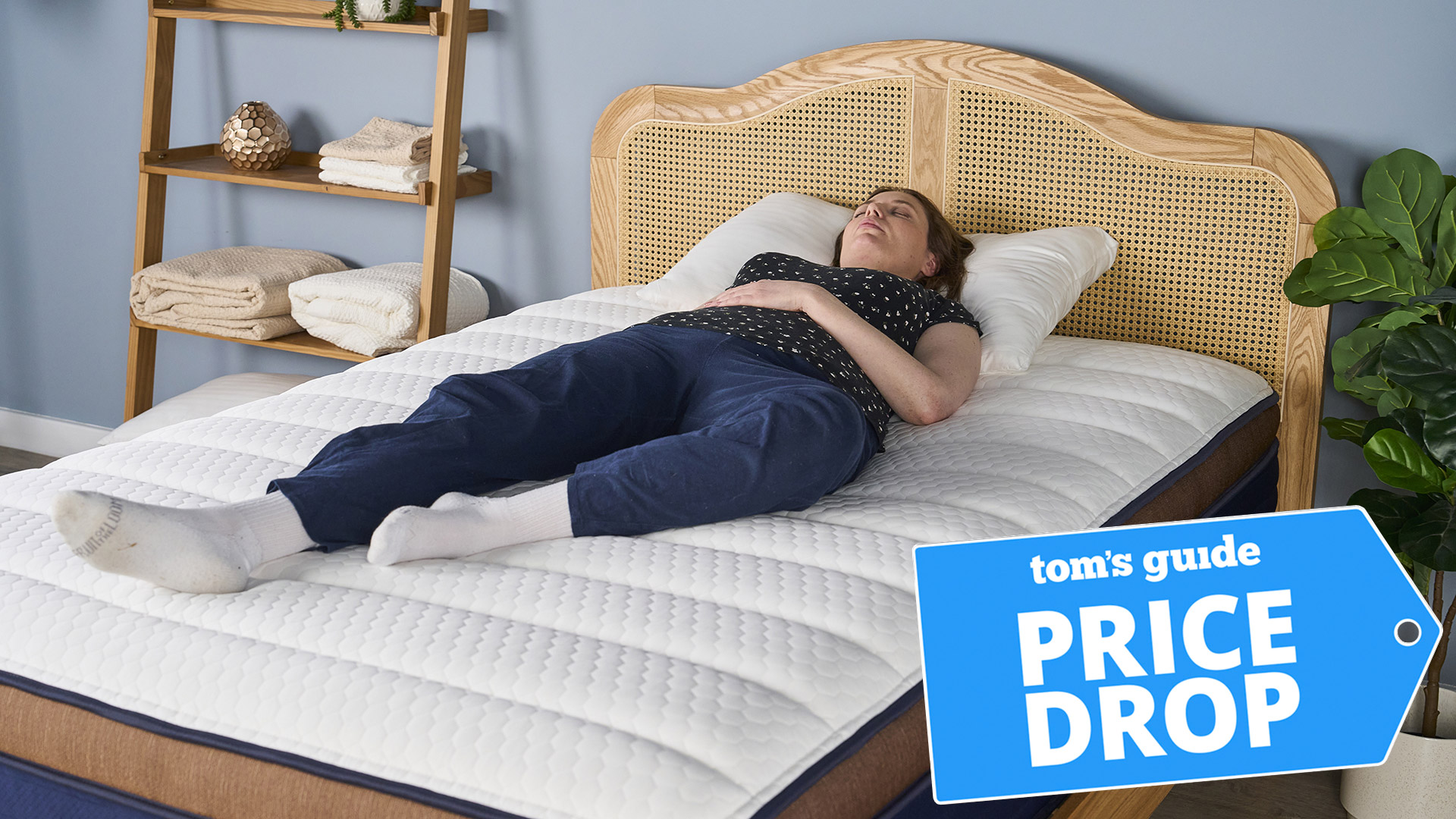 A woman lying on the Brooklyn Bedding CopperFlex Pro Hybrid mattress in a bedroom, with a Tom's Guide badge overlaid saying "PRICE DROP"