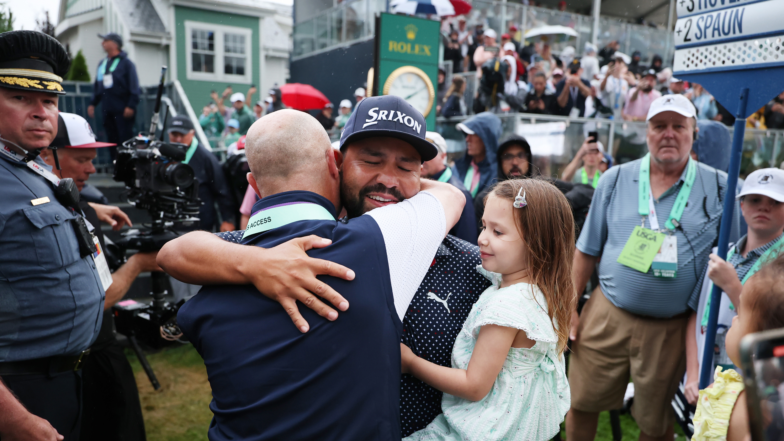 JJ Spaun holds his daughter and hugs his coach after winning the US Open while a TV camera films in the background 