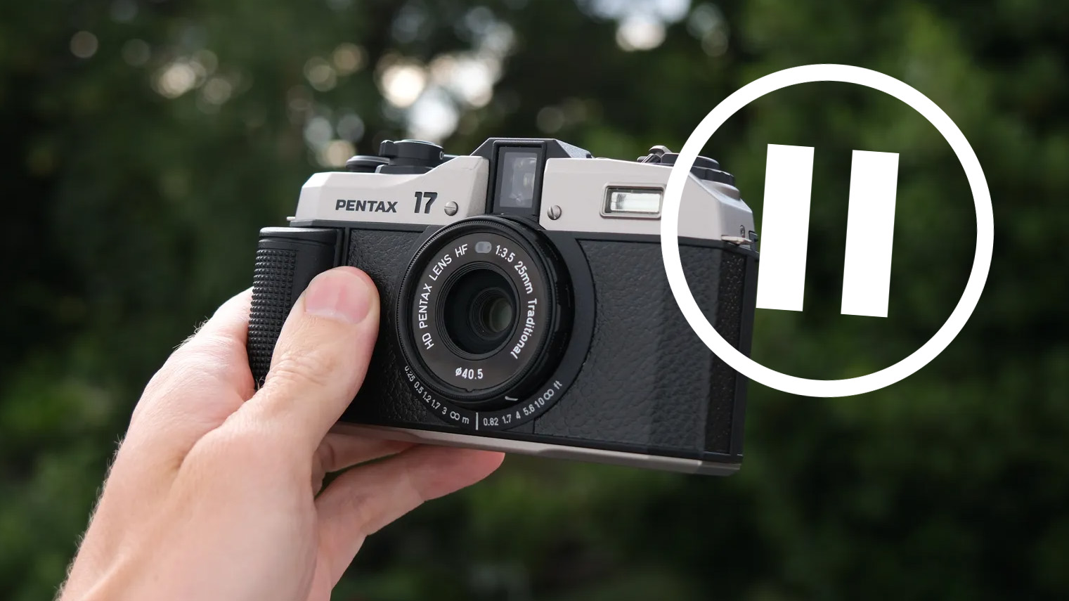 A Pentax 17 film camera held in a hand outside next to pause symbol 
