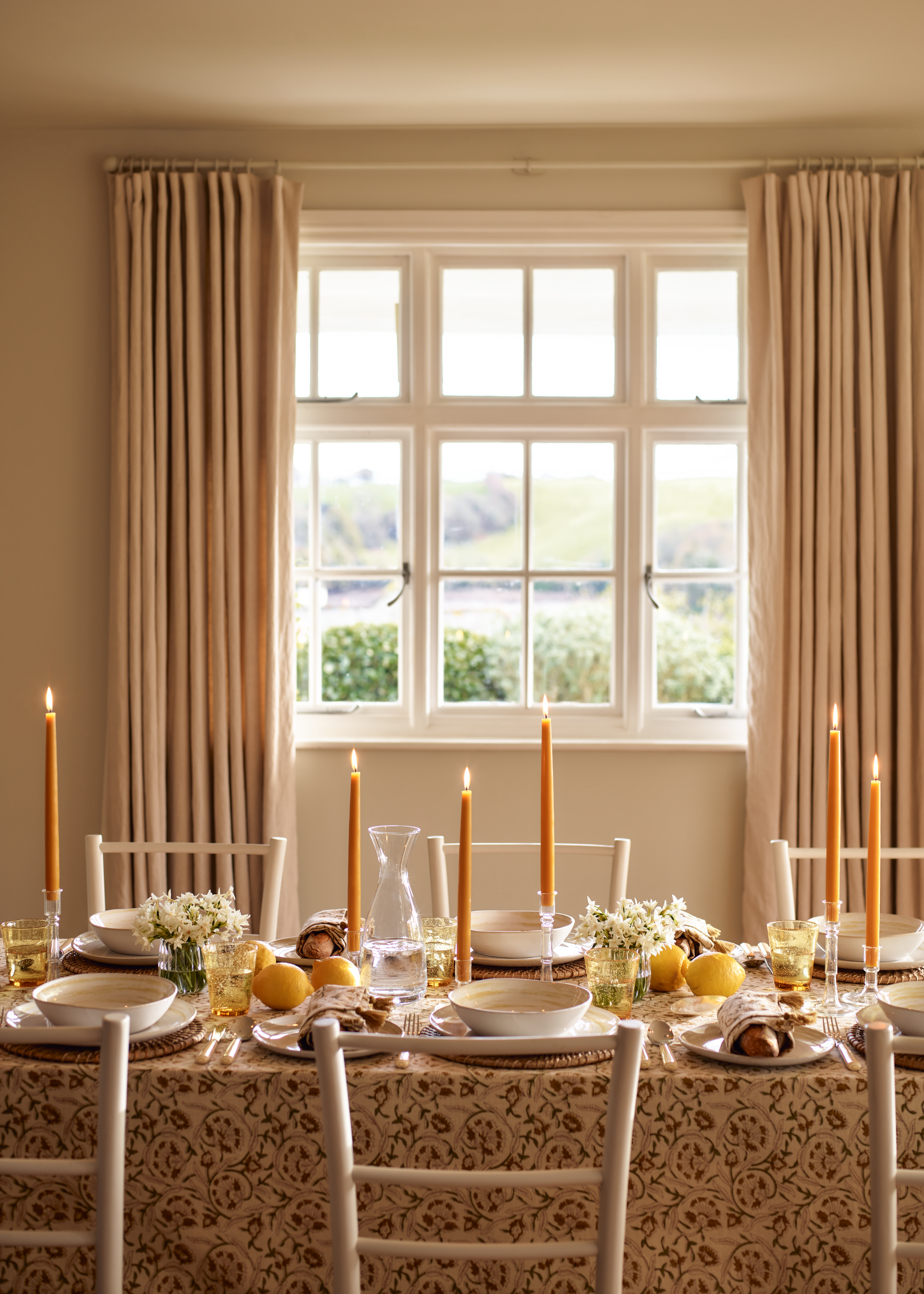 A table setting with orange candles, lemons, and a patterned tablecloth