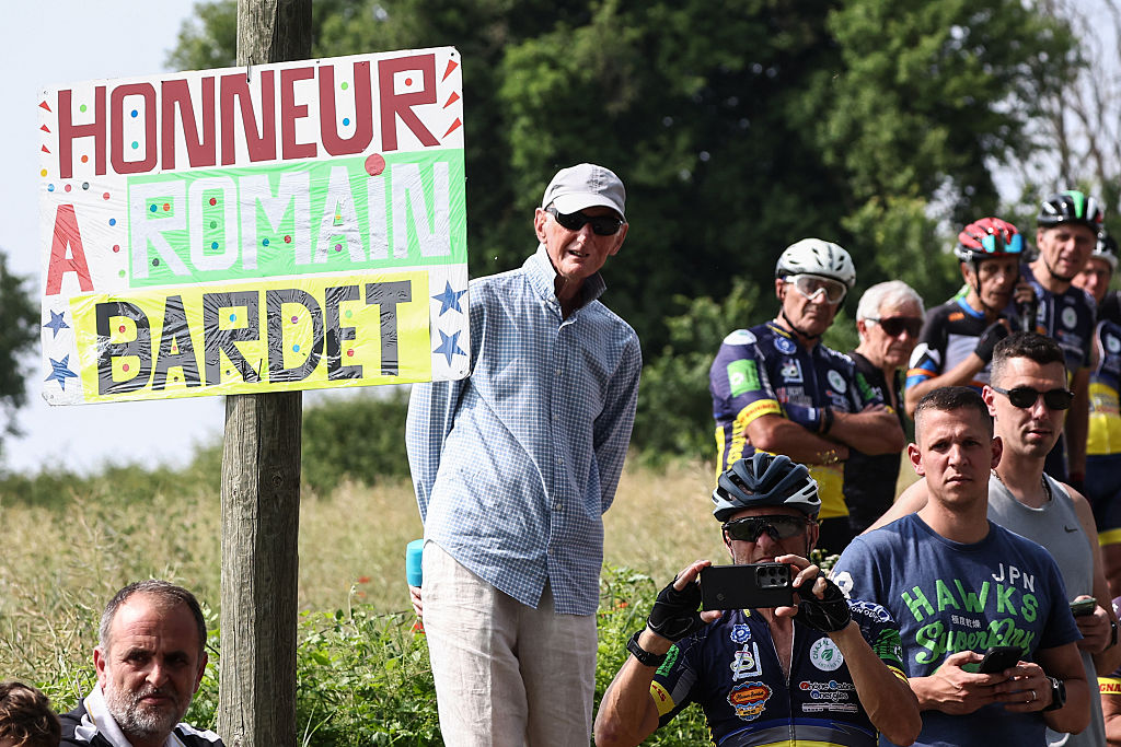 Spectators stand on the side of the road next to a placard reading &quot;honor to Romain Bardet during the 3rd stage of the 77th edition of the Criterium du Dauphine cycling race, 207,2 km between Brioude and Charantonnay, on June 10, 2025. (Photo by Anne-Christine POUJOULAT / AFP)