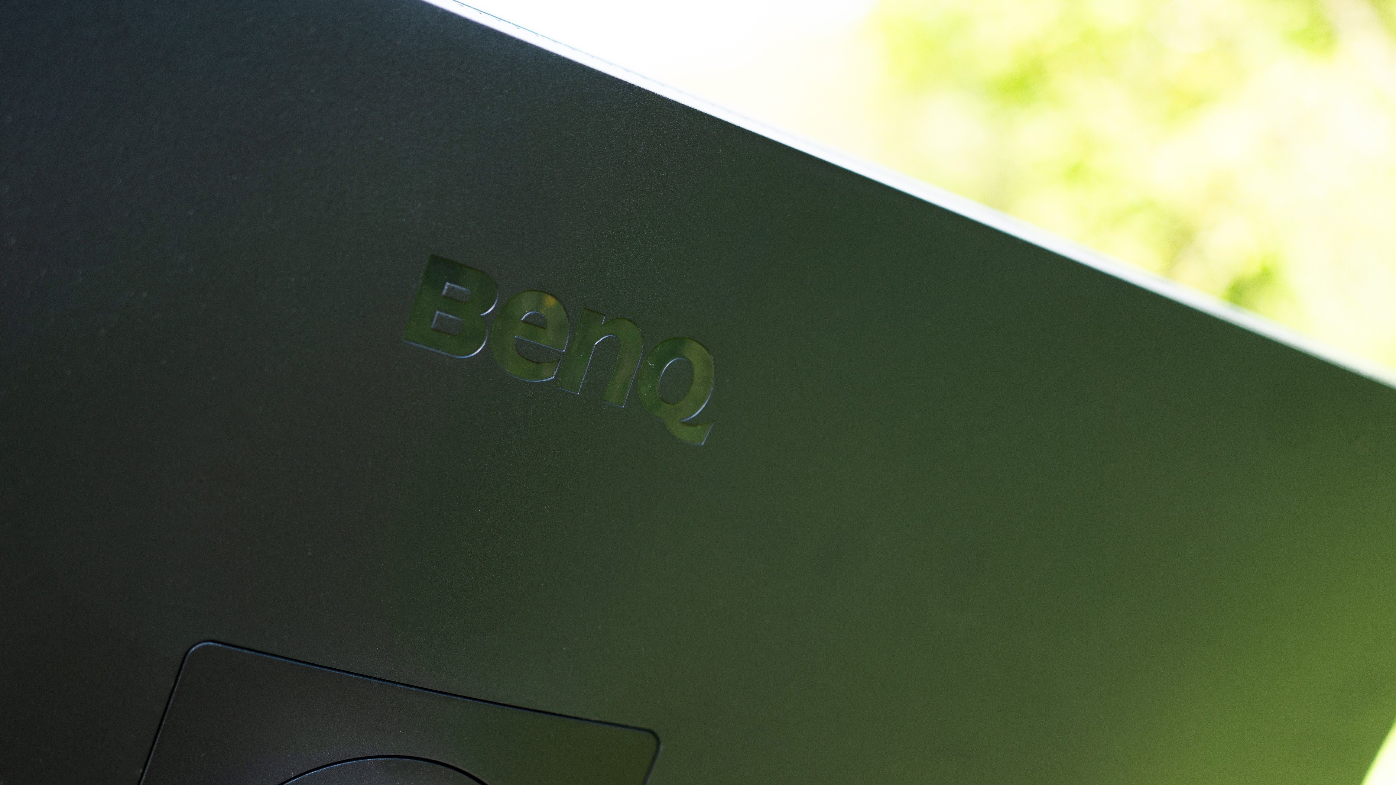 A black BenQ PD3225U monitor sitting on grass in sunshine