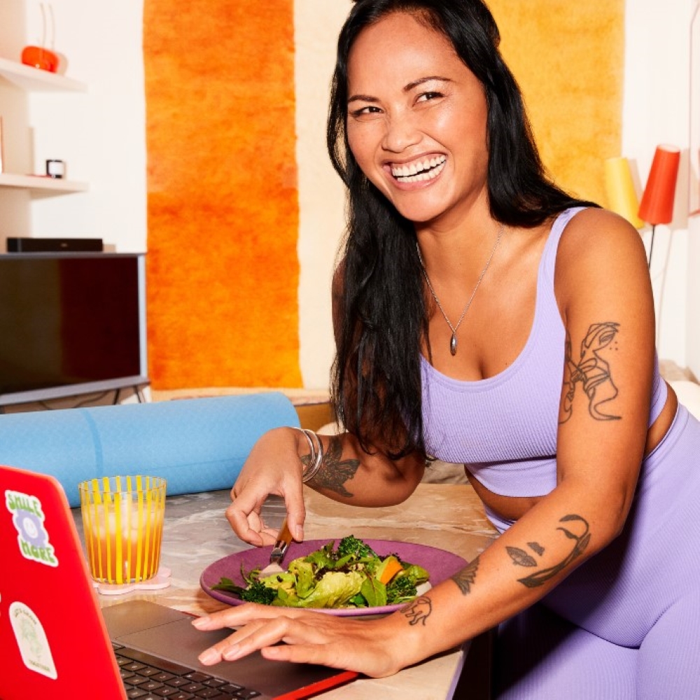 Young woman in purple gym gear with salad and laptop in front of her