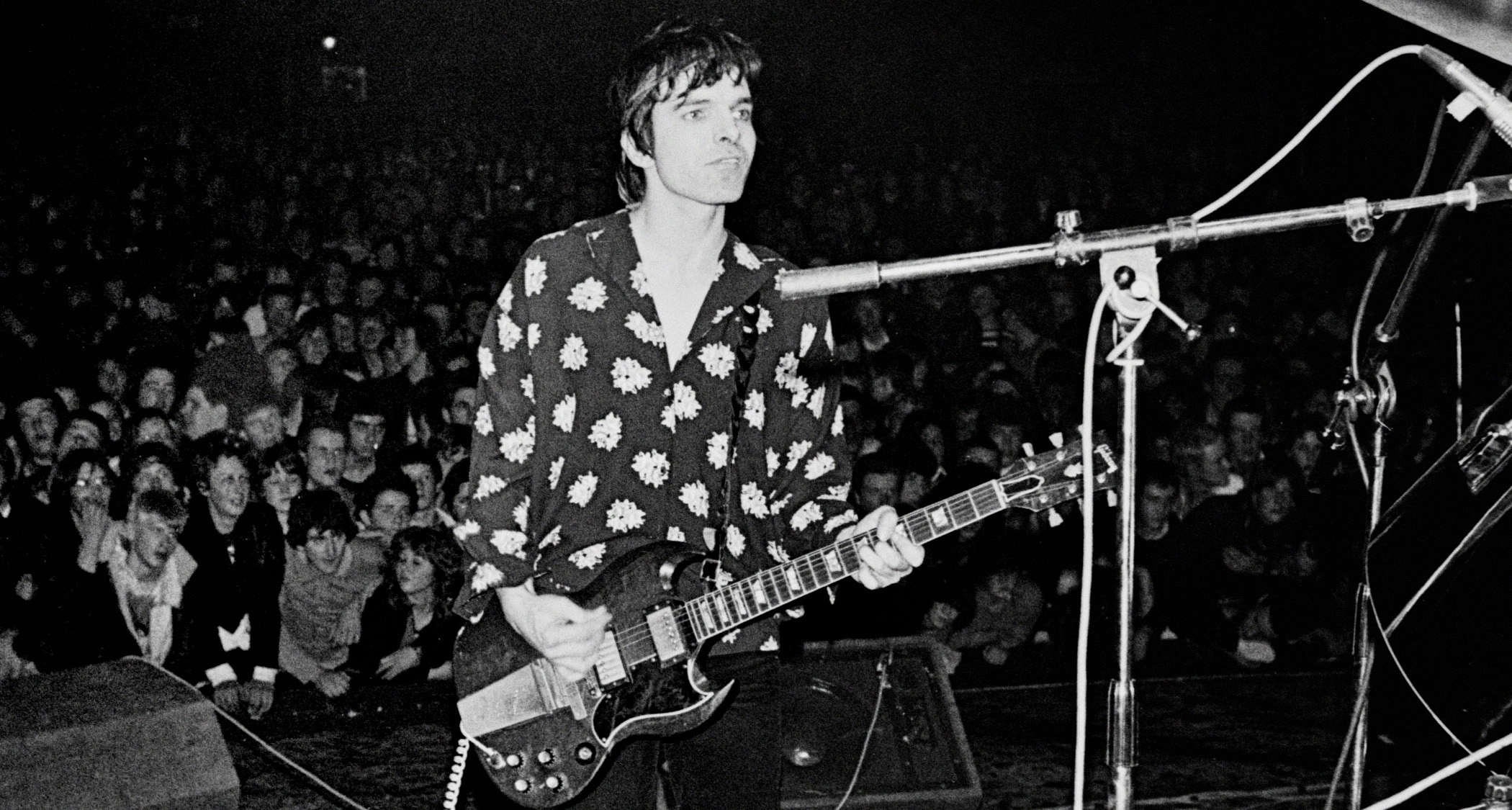An archive black-and-white live shot of The Damned&#039;s Brian James, who wears a floral-pattern shirt and plays a Gibson SG with vibrato as the UK punk pioneers play their farewell gig.