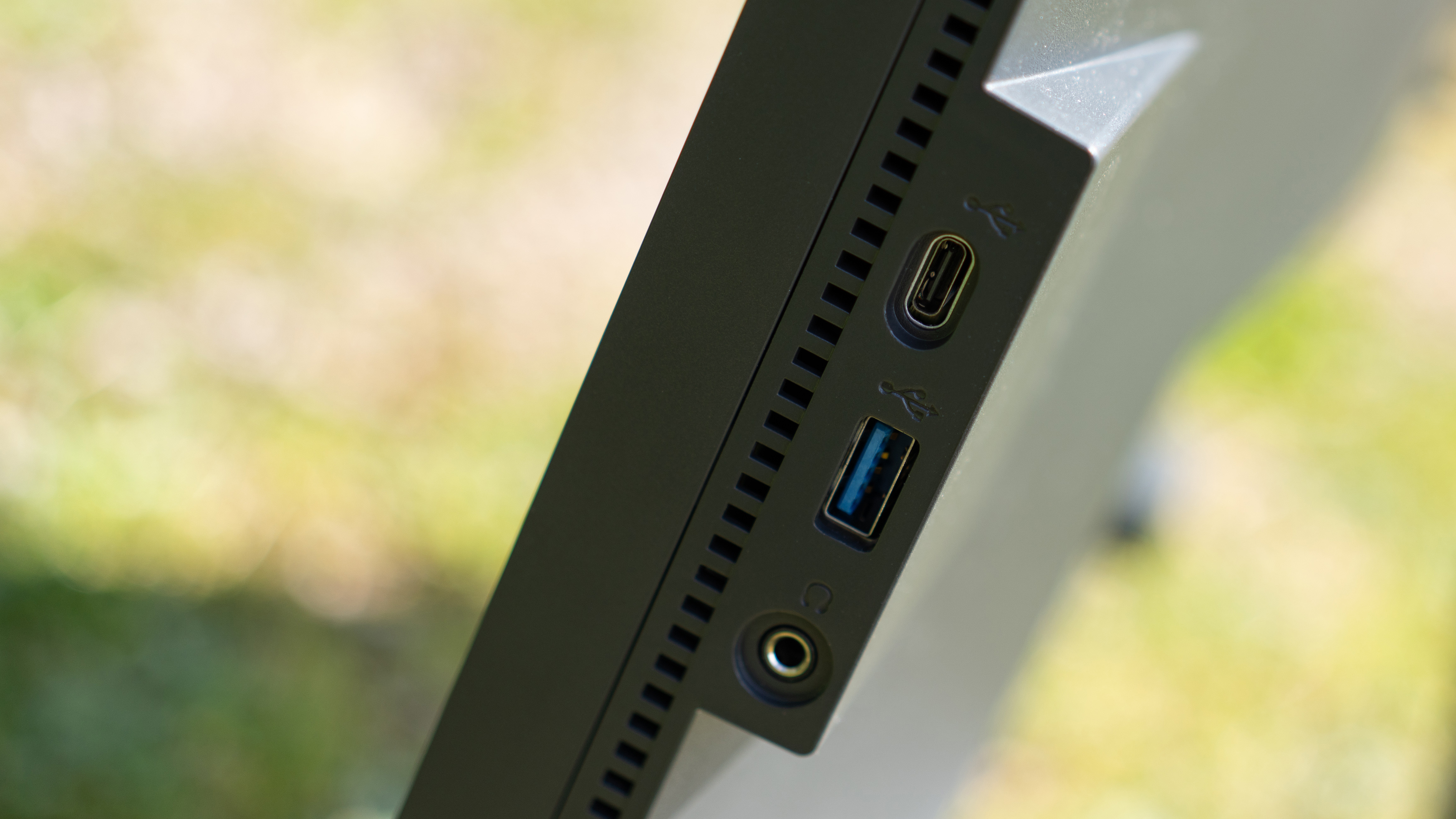 A black BenQ PD3225U monitor sitting on grass in sunshine