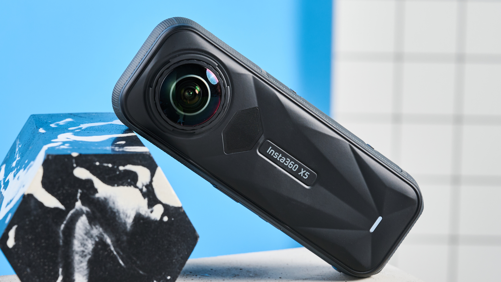 The Insta360 X5 on its side resting on a marble block, against a blue background