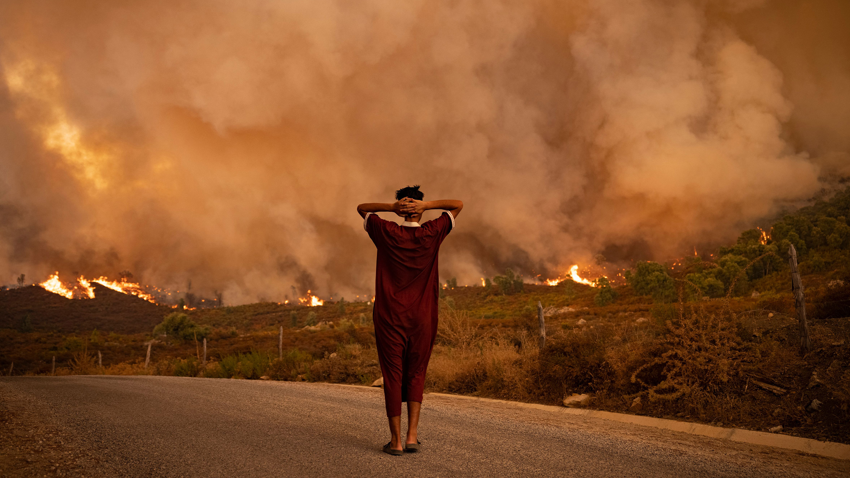A woman looks at wildfires tearing through a forest in the region of Chefchaouen in northern Morocco on Aug. 15, 2021. One of the effects of global warming will be more heat waves in some areas, a risk factor for wildfires.