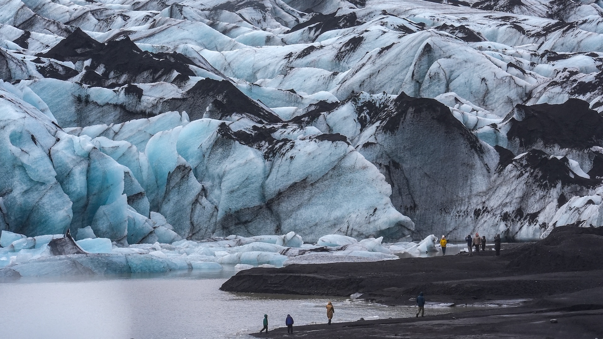 Tourists look at a large glacier and the lake it's melting into.