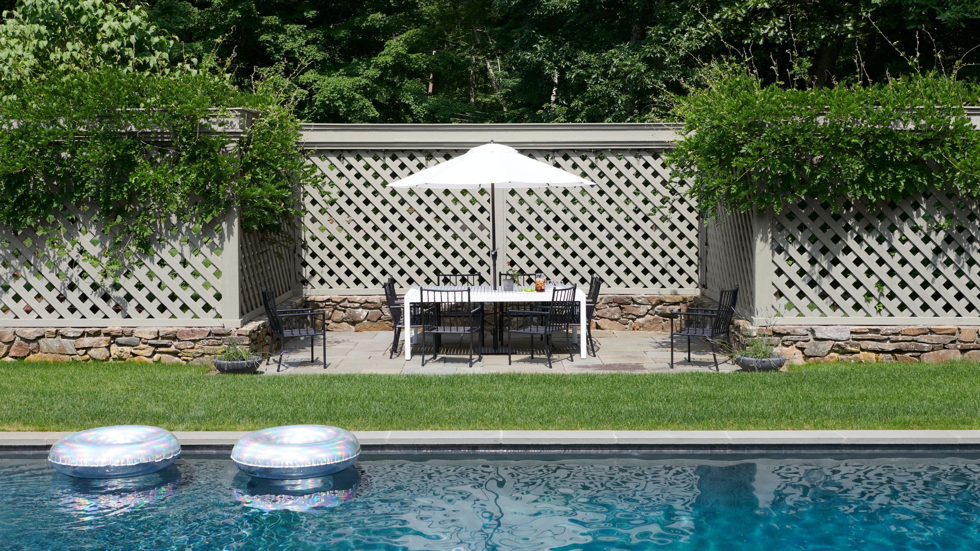 A garden with a large swimming pool and a outdoor dining area and garden fence painted in gray 