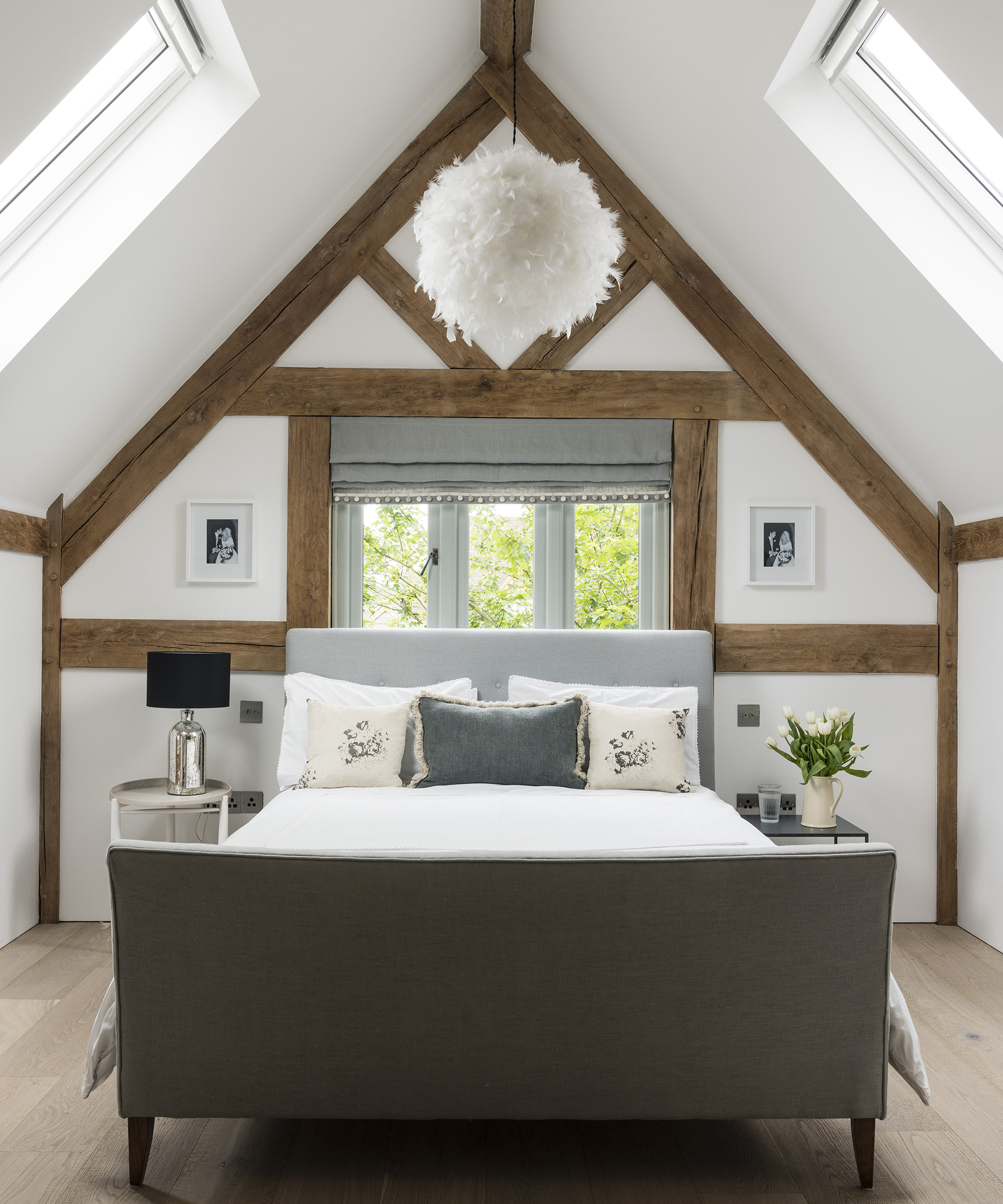 A double bed in the loft portion of an oak frame home. There are exposed beams and neutral walls