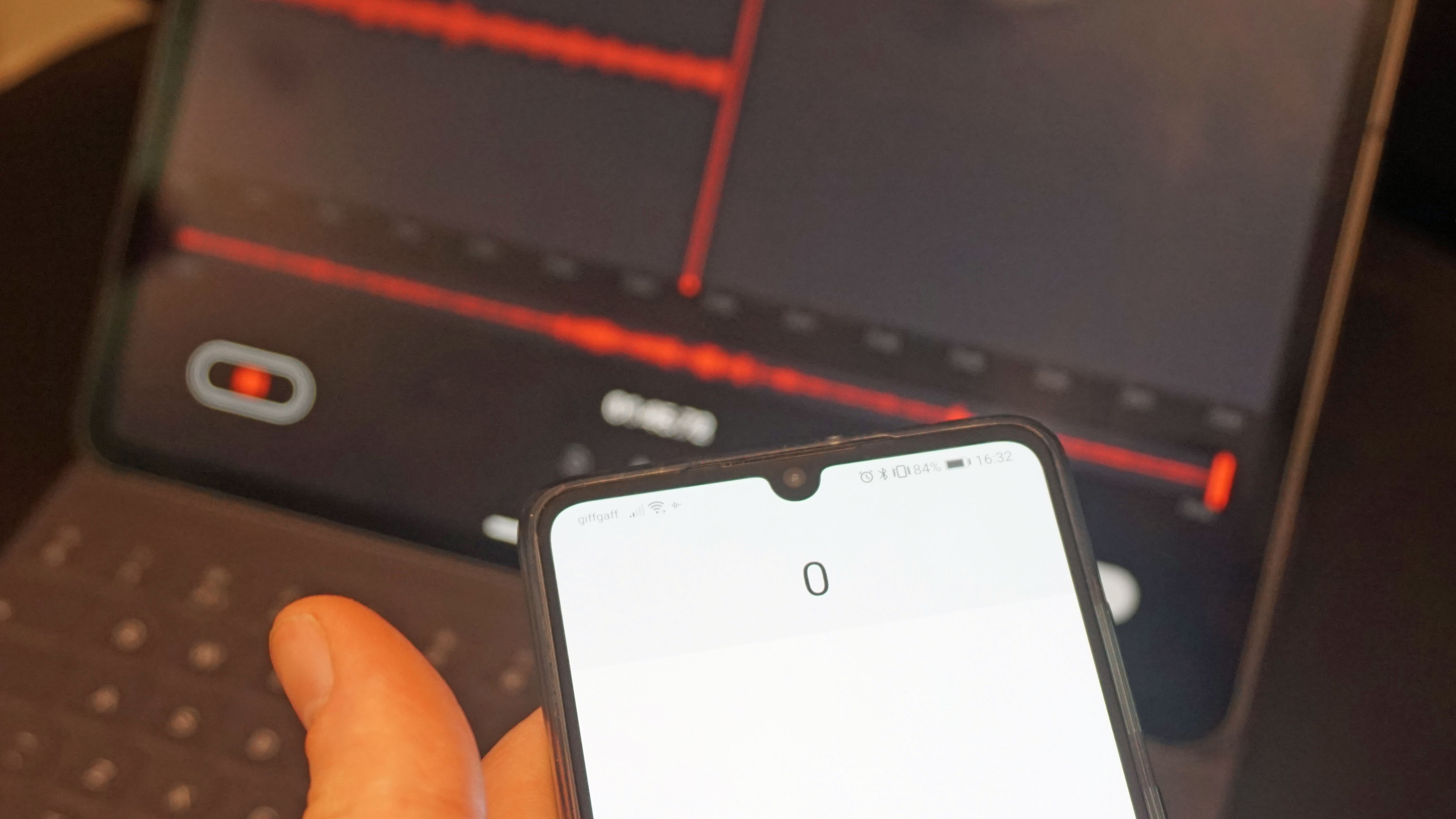 Hand holding phone with laptop recording software in background