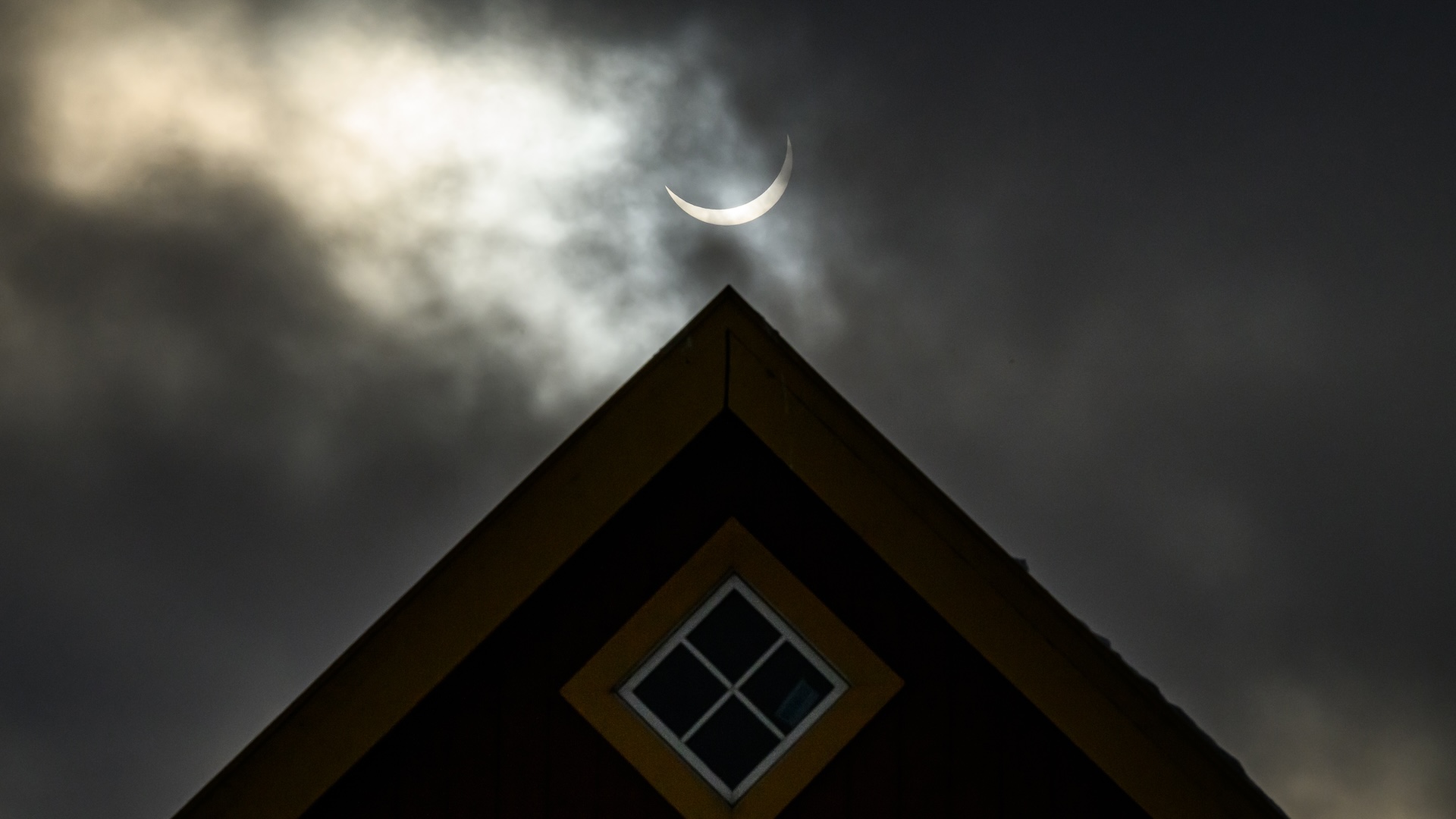 The sun in a narrow crescent during an eclipse is centered above the peak of a home's roof