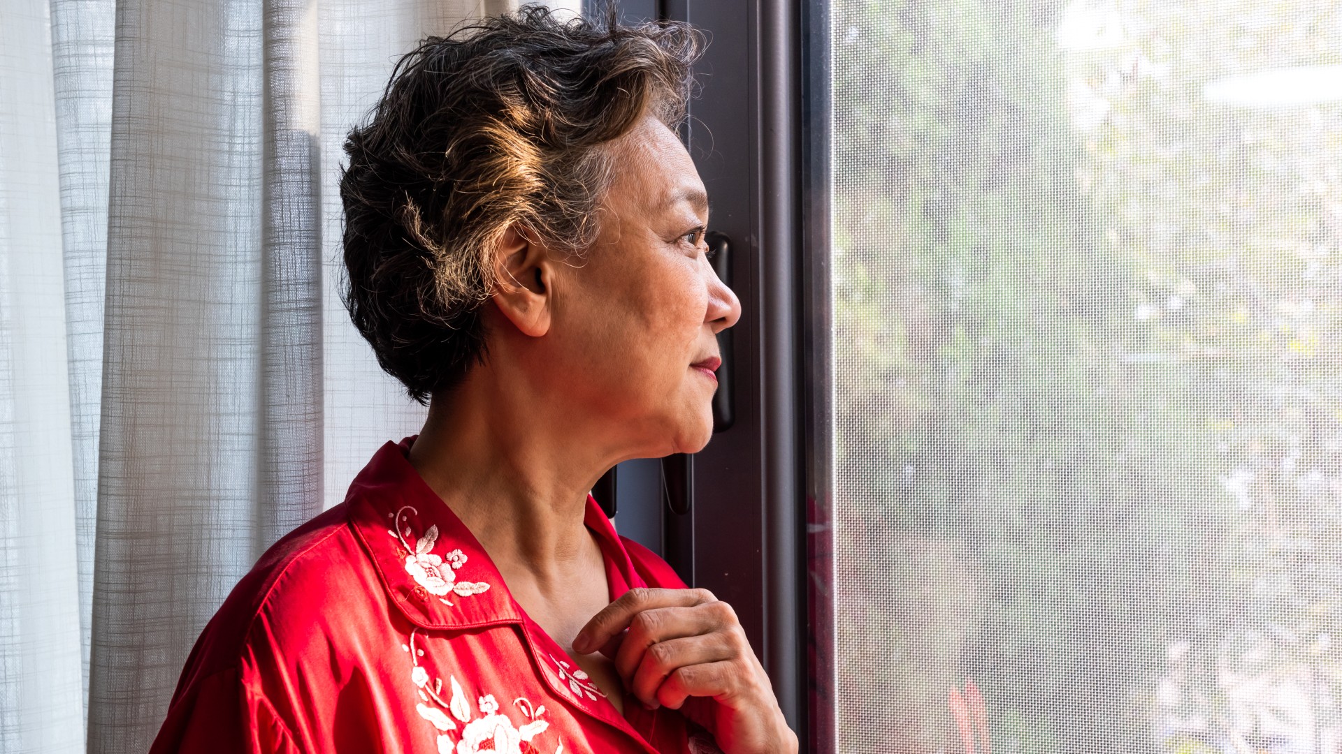 Older woman is shown staring out of a window
