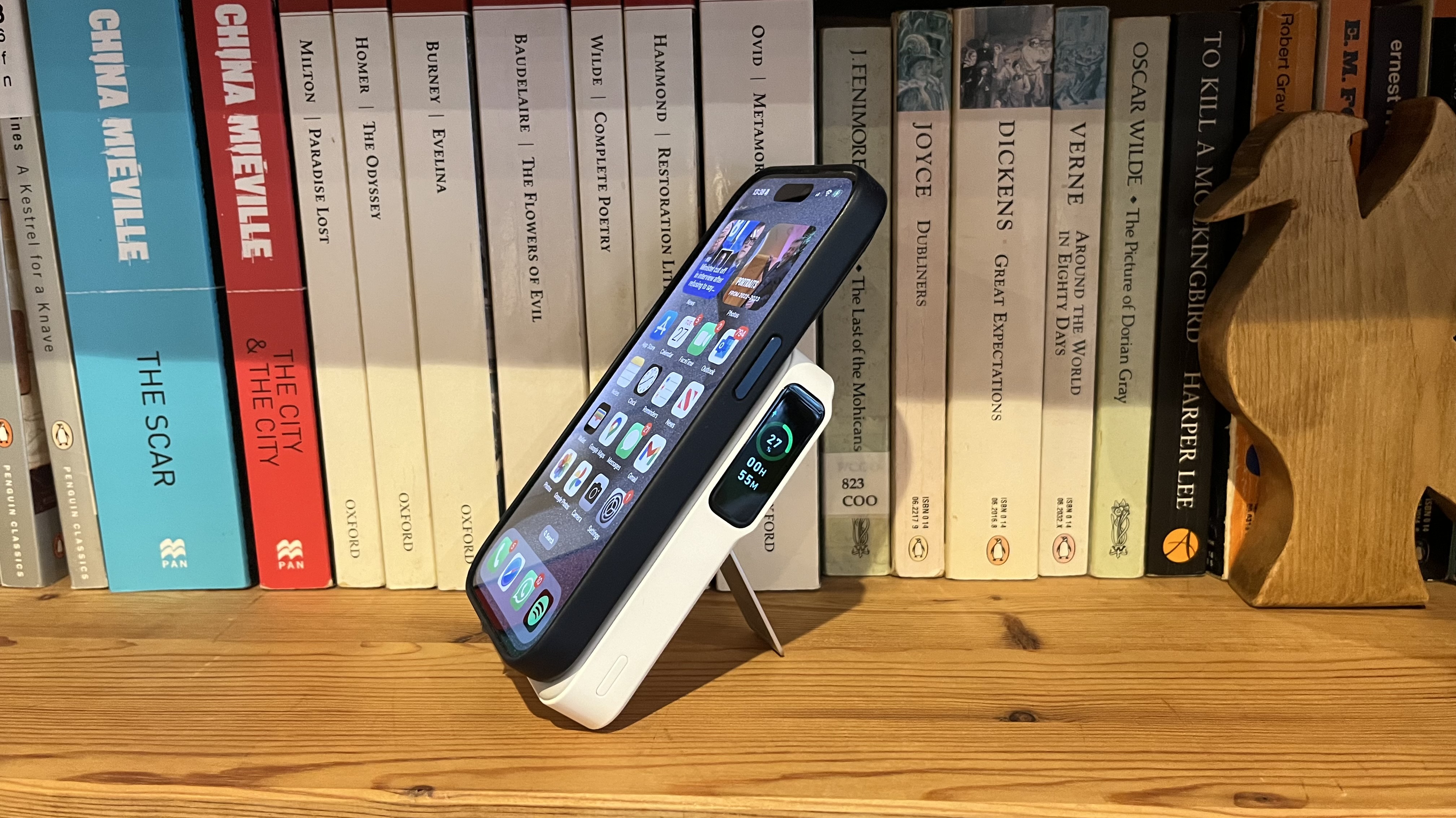 The Anker MagGo Power Bank (10K) connected to an iPhone 15 Pro on a wooden bookshelf