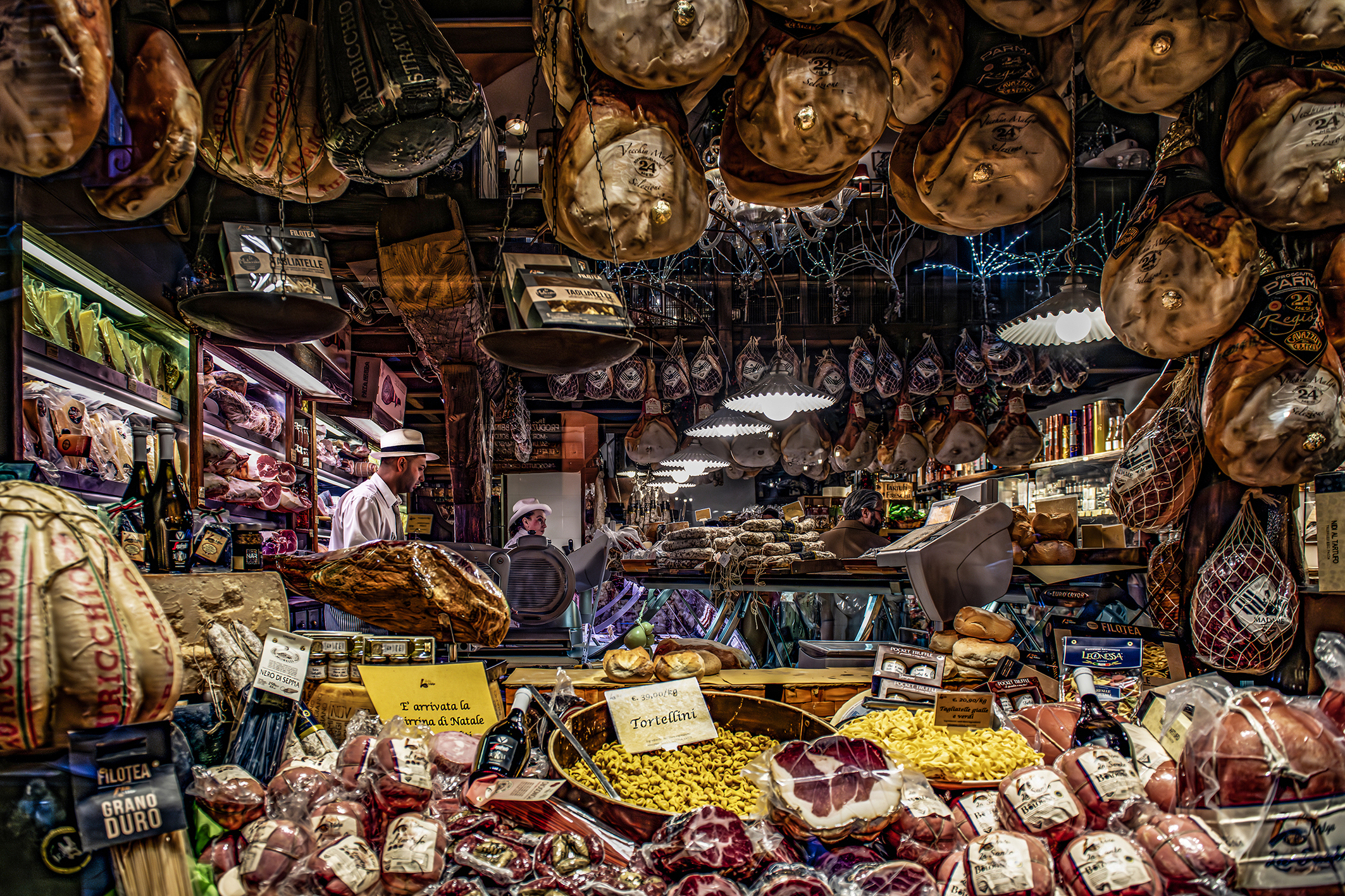 A bustling market scene filled with hanging cured meats, cheeses, and fresh pasta, showcasing a variety of local delicacies on display