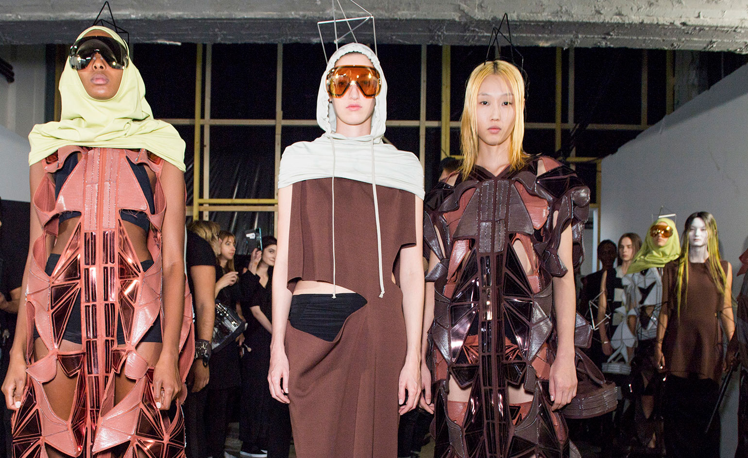 Models wear rust dress with green balaclava, light blue and brown dress, and brown dress with black underwear