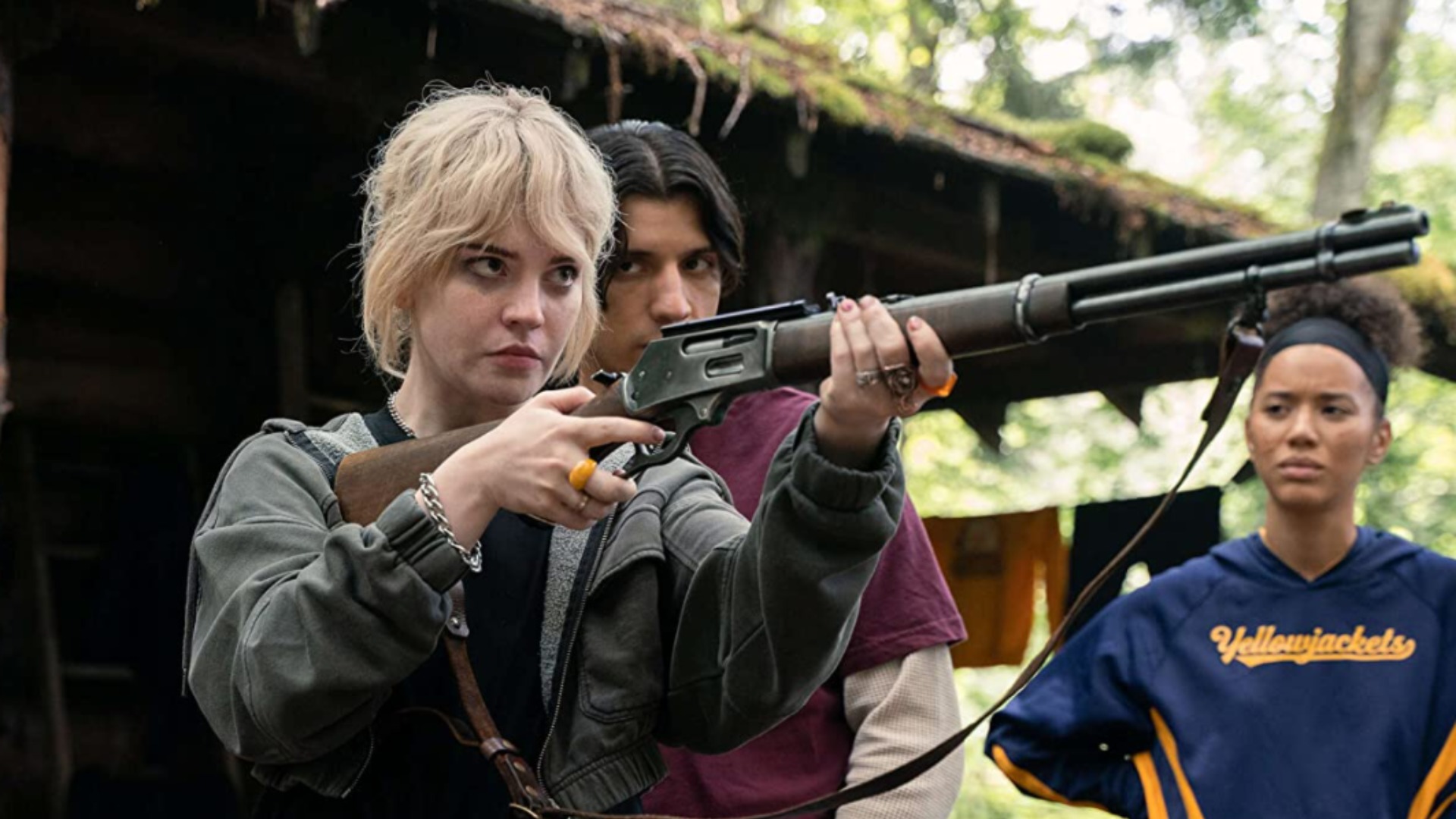 Sophie Thatcher as teenage Nat aims a shotgun, while her friends watch on, in Yellowjackets.