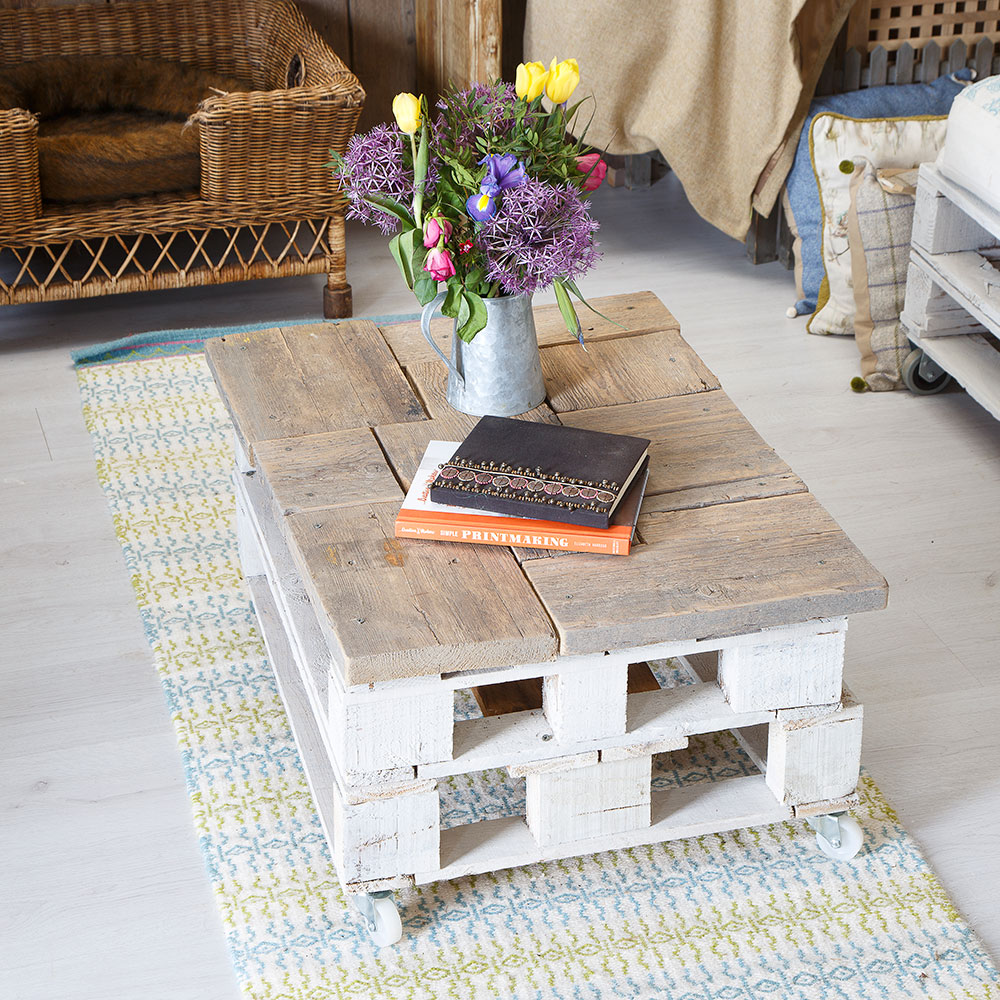 Pallet coffee table on patterned rug next to wicker chairs