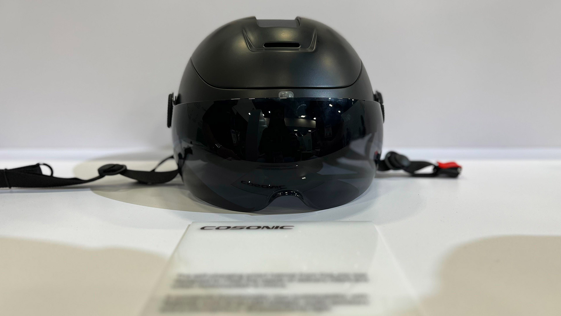 A helmet with a dark visor sits on a table in front of an info sign.