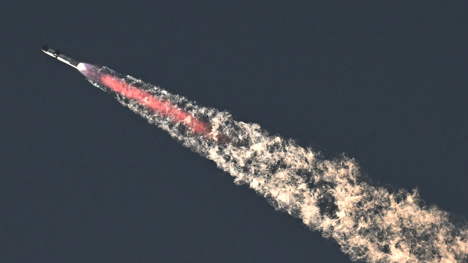 Photo of starship flying through the sky with a plume of fire and smoke