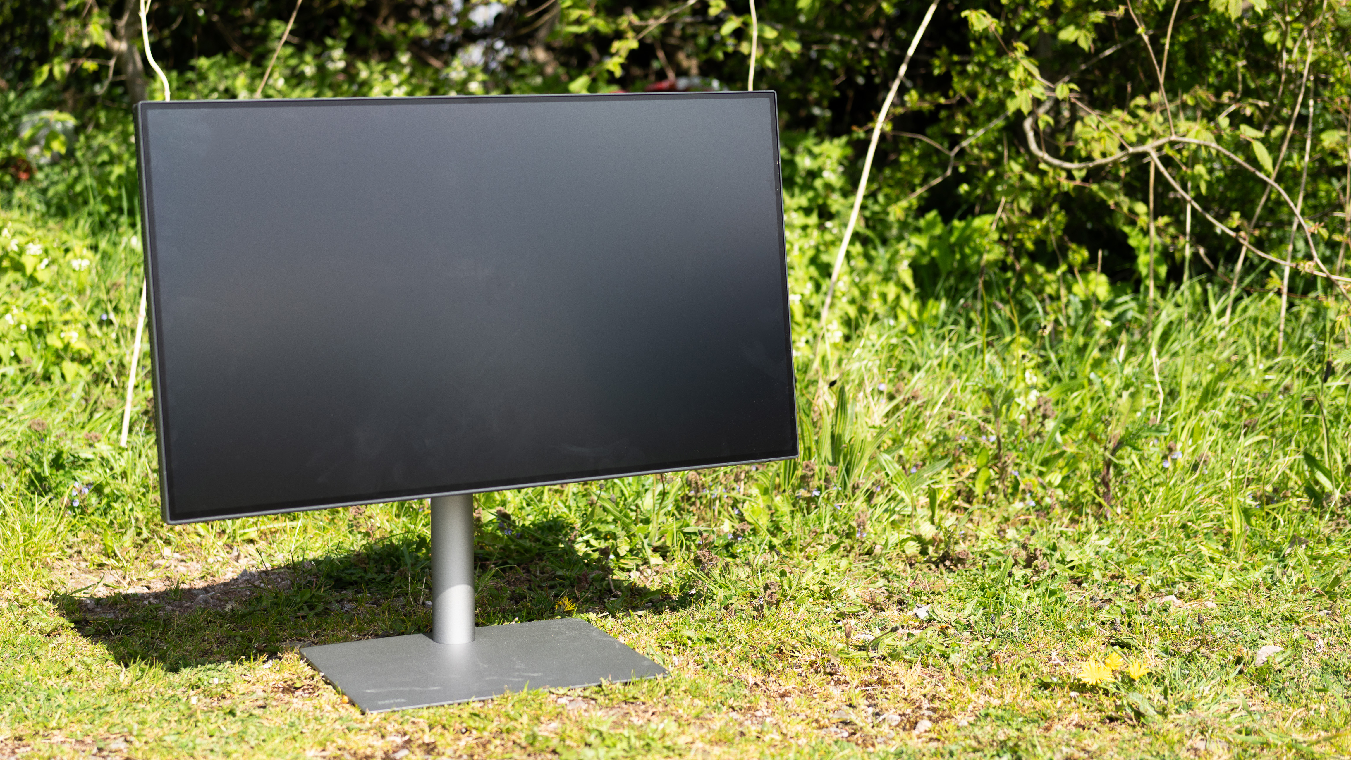 A black BenQ PD3225U monitor sitting on grass in sunshine