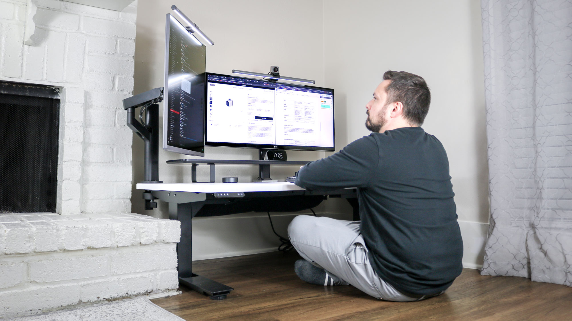 A person sitting on the floor while using the Uppeal 2 Leg Desk with a multi-monitor setup