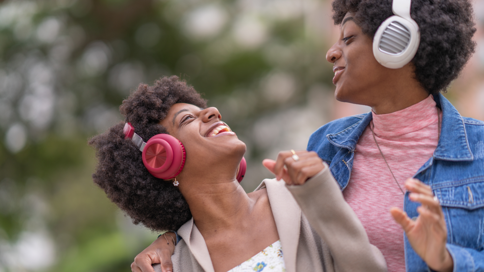 African American twin sisters wearing headphones enjoying music in the park, wearing jackets because of the cold.