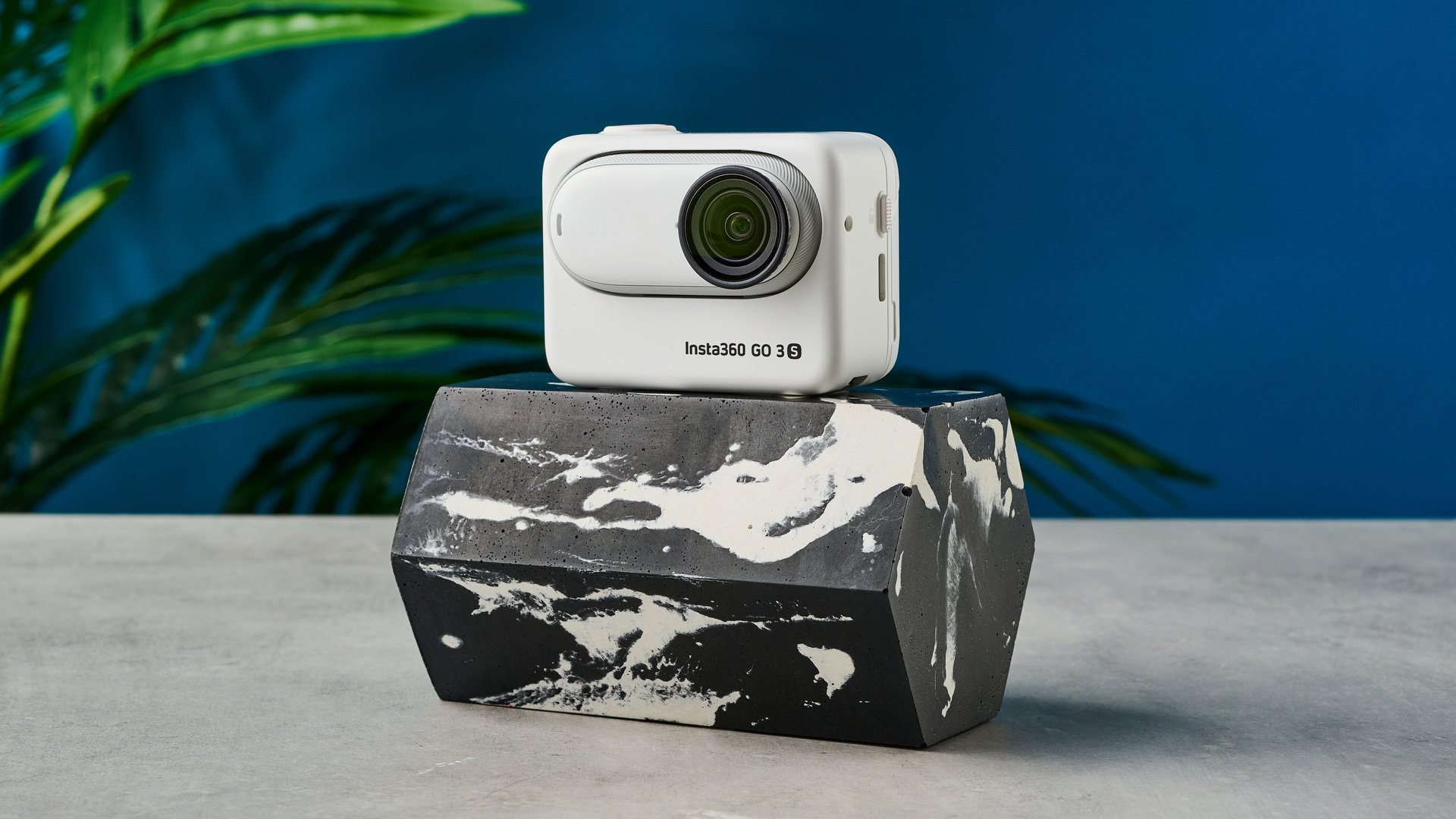 A photo of the Insta360 Go 3S on a black and white marble plinth with a blue background.