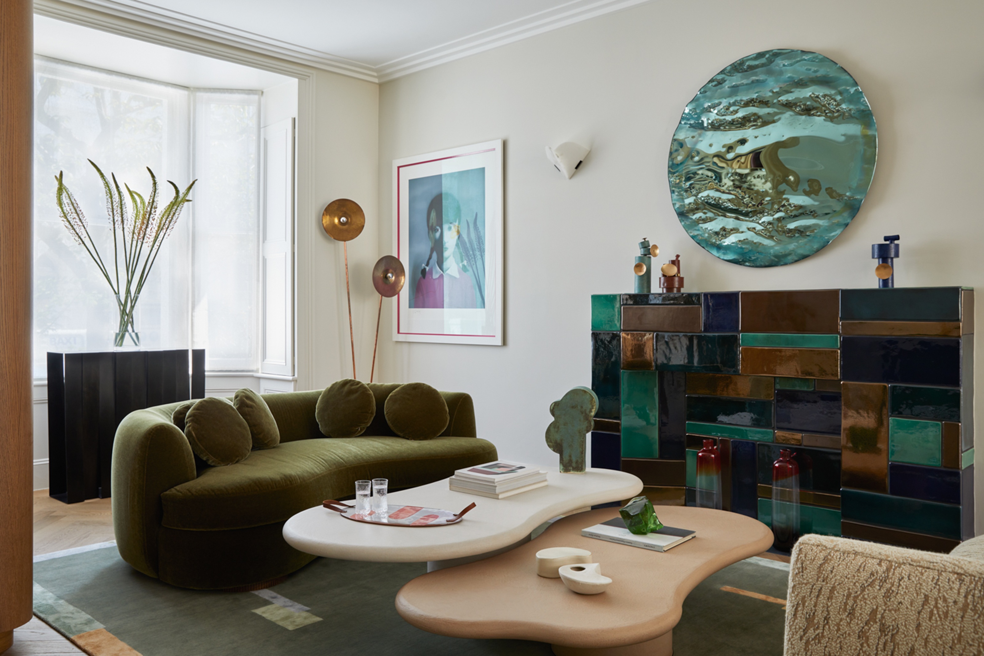 a living room with a green rounded sofa, a tiled colorful fireplace and a teal mirror